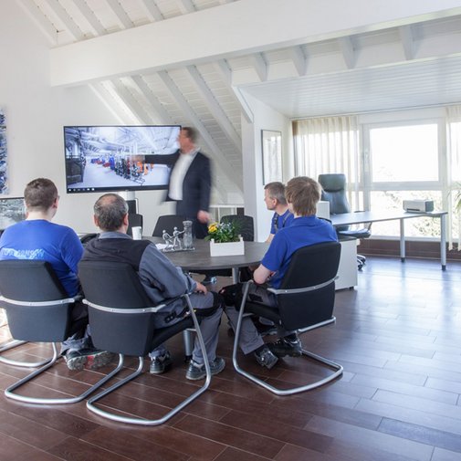 Der Konferenzraum ist hell erleuchtet, mit großen Fenstern und einem Bildschirm, auf dem technische Informationen angezeigt werden.