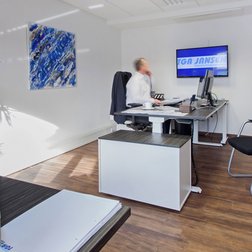 Ein moderner Büroraum mit einem Schreibtisch, einem Computer und einem Mitarbeiter, der konzentriert arbeitet.