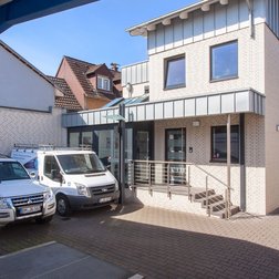 Die Fassade des Unternehmensgebäudes zeigt helle Ziegelsteine und große Fenster, während Lieferwagen im Vordergrund parken.